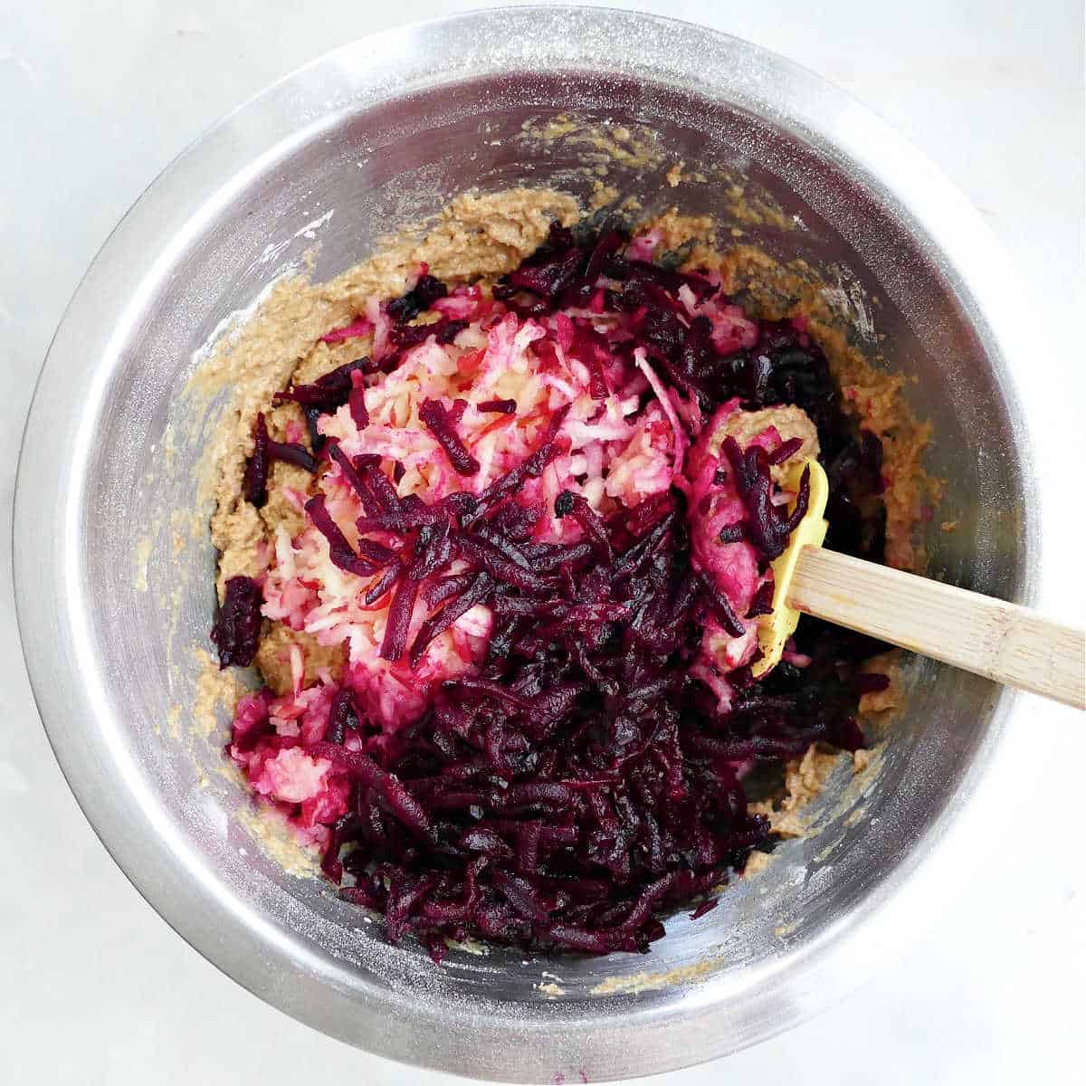 shredded beets and apples being stirred into muffin batter with a rubber spatula