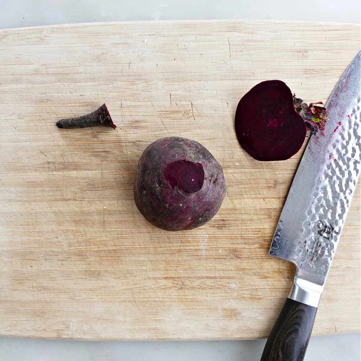 a trimmed beet on a cutting board with a chef's knife