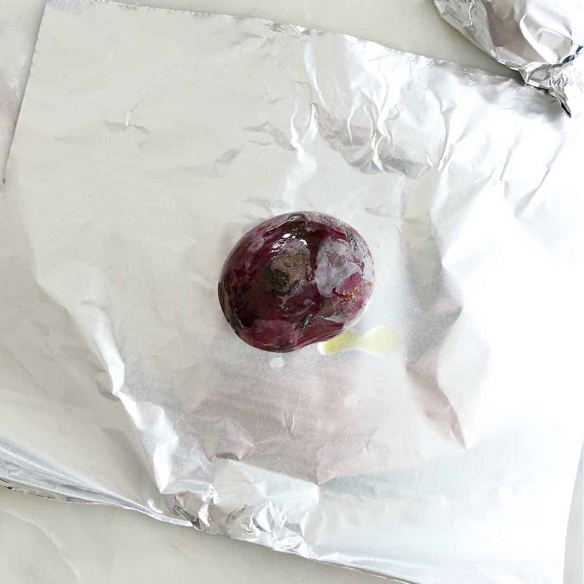 a red beet rubbed with oil on a piece of aluminum foil