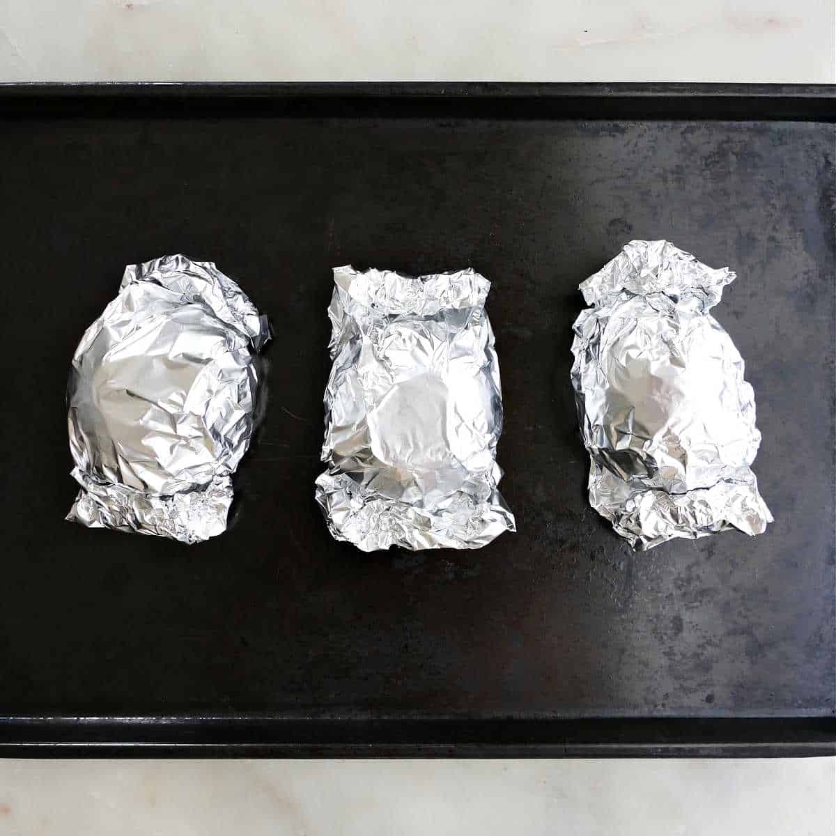 3 foil packets of beets prepared for roasting on a baking dish