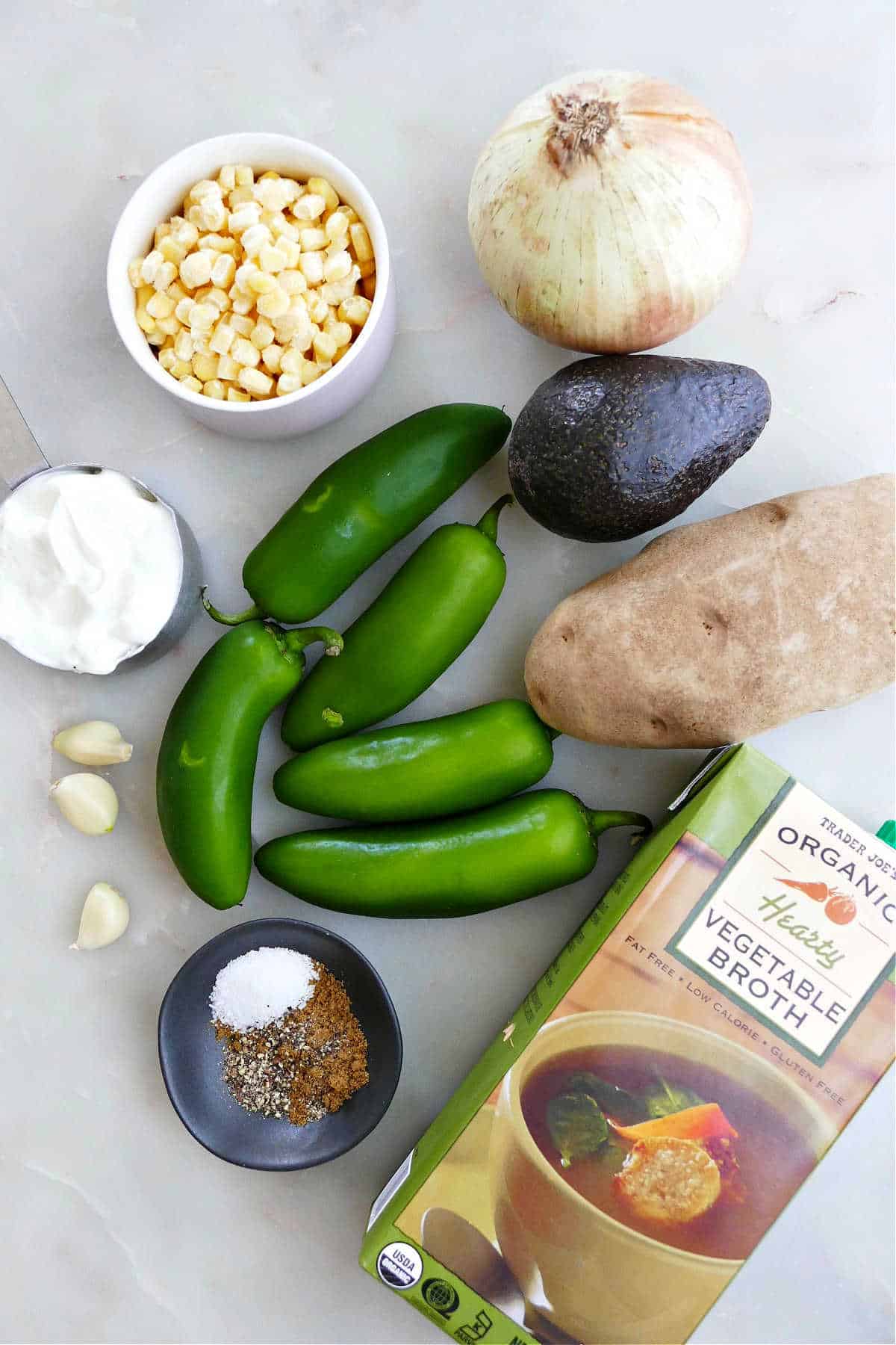 corn, onion, avocado, potato, vegetable broth, jalapeños, spices, garlic, and yogurt on a counter