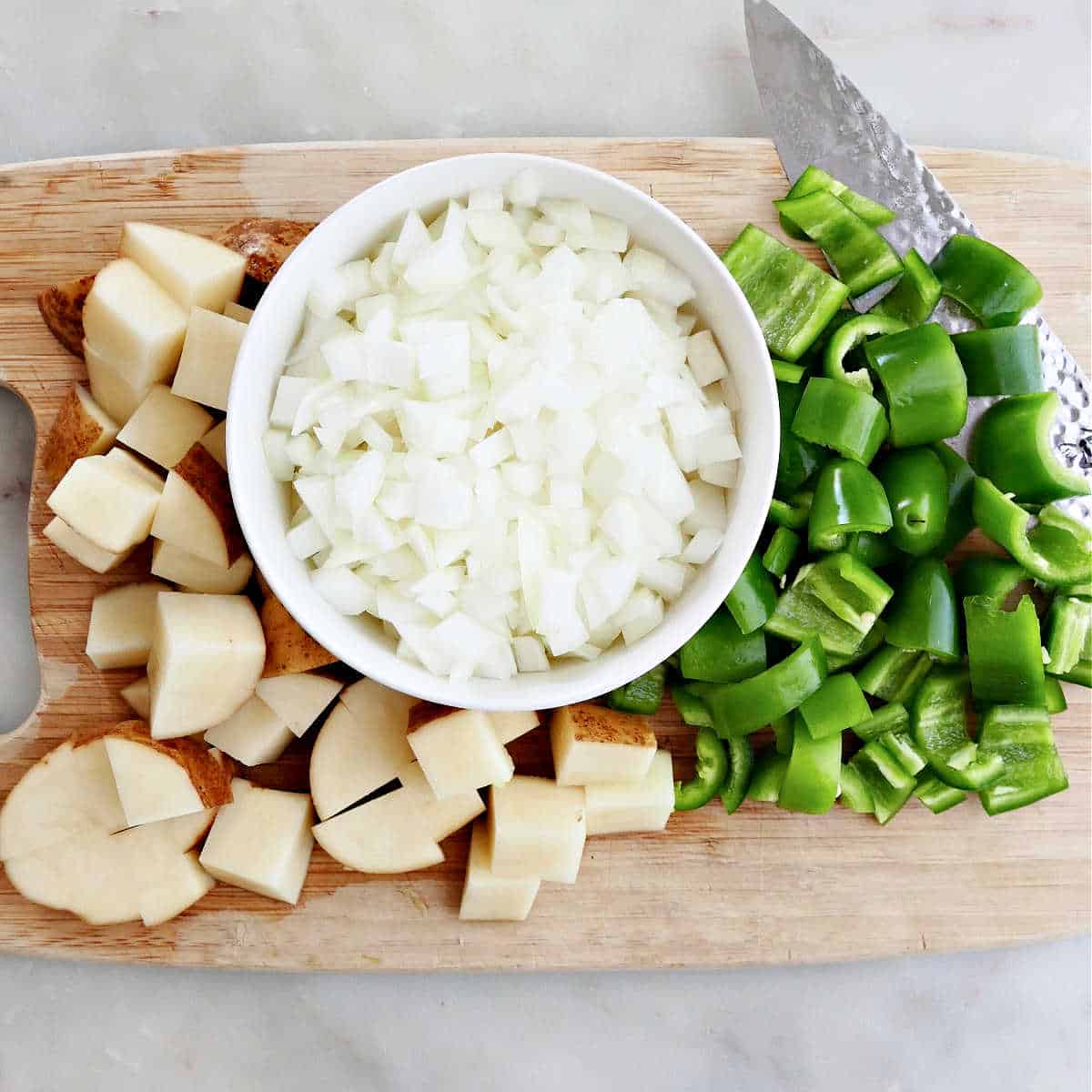sliced potatoes, onion, and jalapeños on a cutting board next to a knife