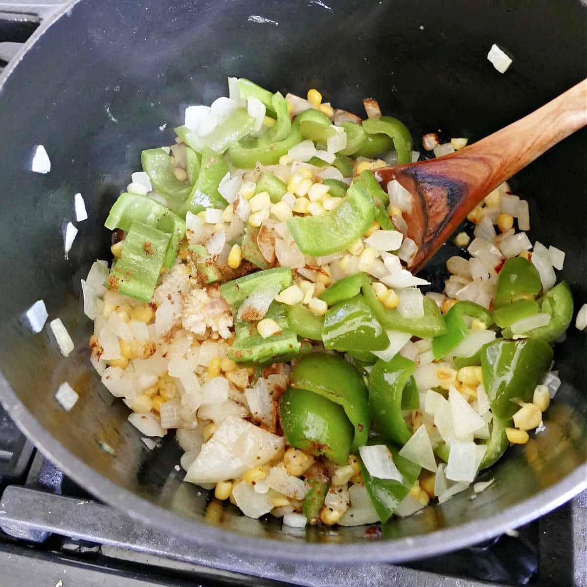 onion, peppers, and corn cooking in olive oil in a skillet