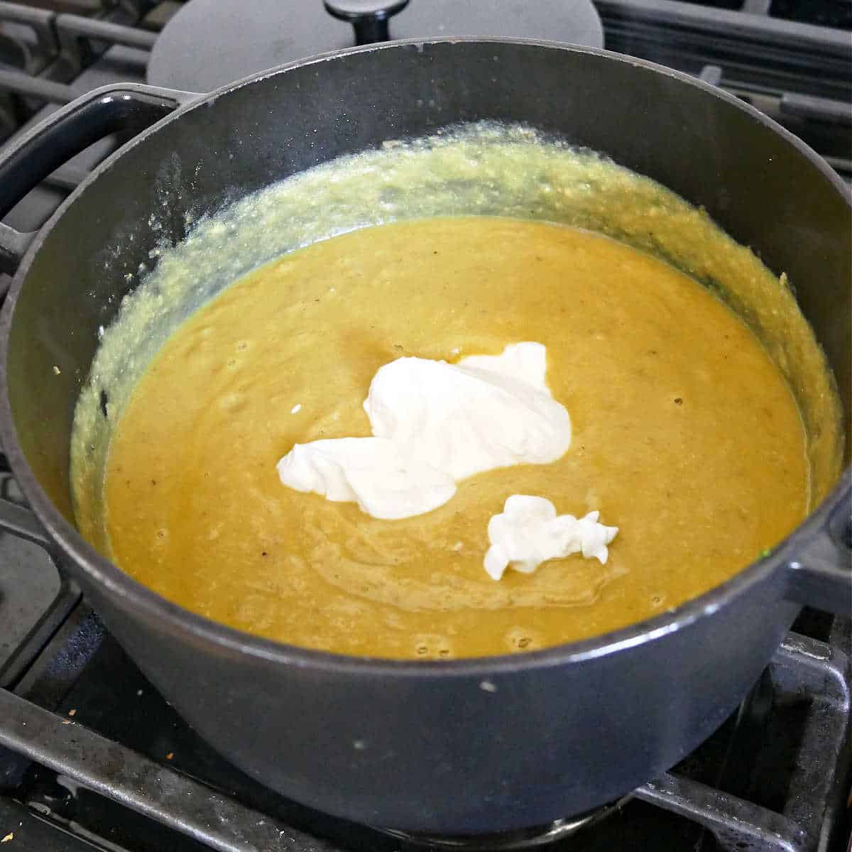 Greek yogurt being added to blended jalapeño soup in a soup pot
