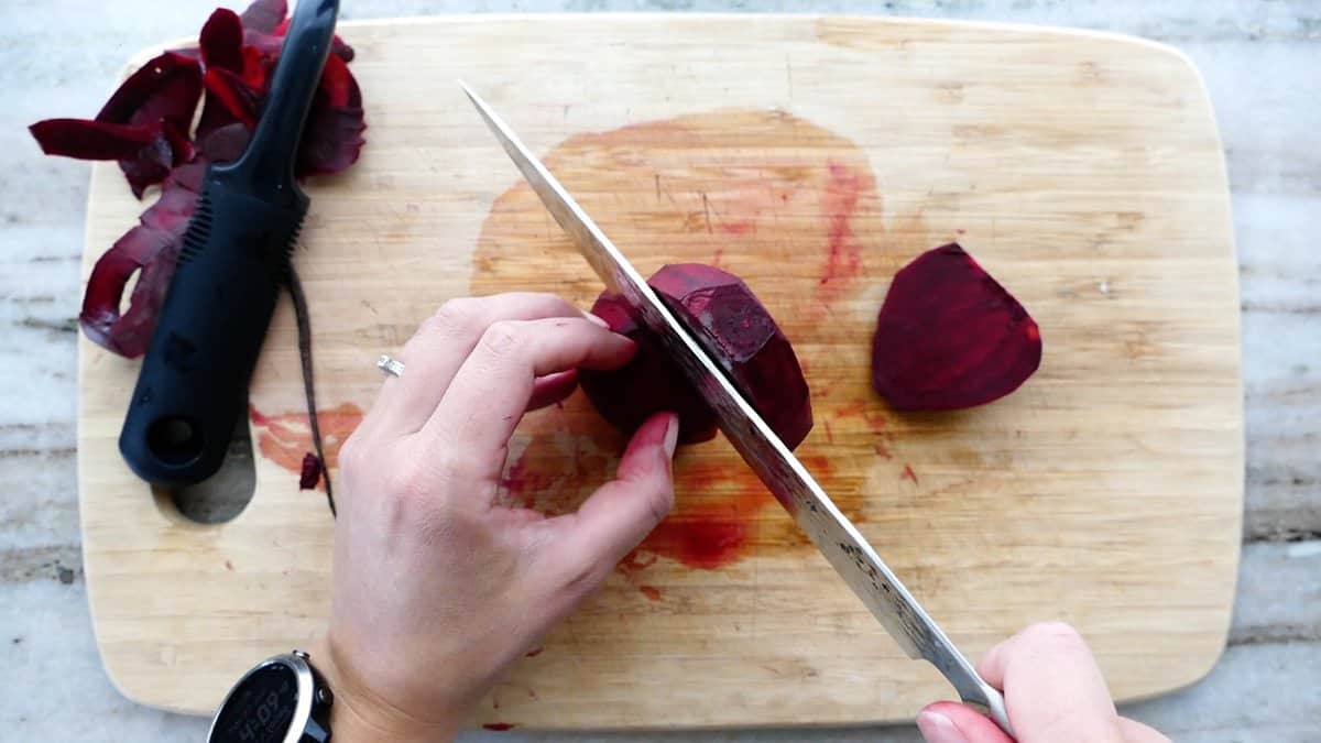 woman slicing beetroot into slices with a chef's knife on a cutting board
