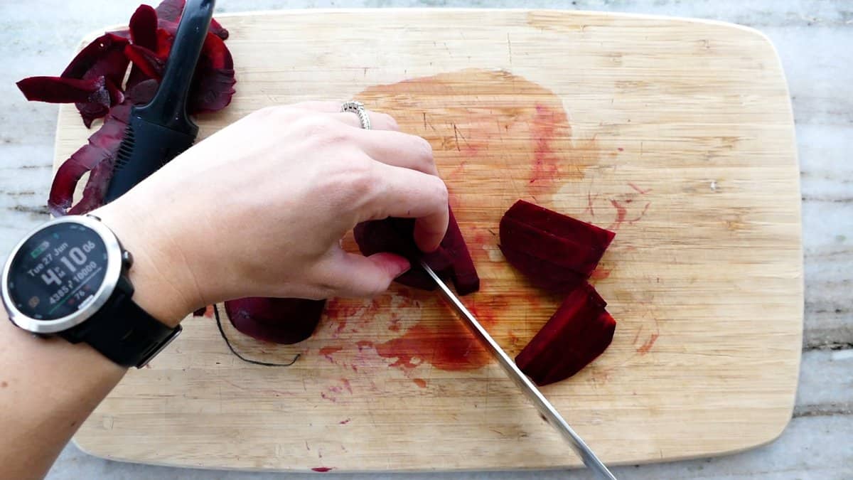 woman cutting beet slices into sticks with a chef's knife on a cutting board