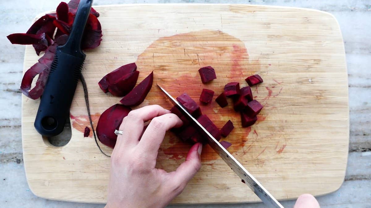 woman cutting beets into cubes with a chef's knife on a cutting board
