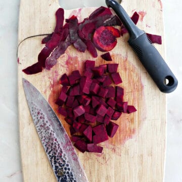 diced beets on a cutting board next to a chef's knife and swivel peeler