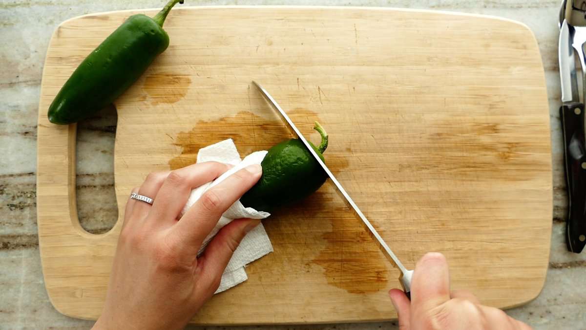 woman trimming off the stem of a jalapeño pepper on a cutting board