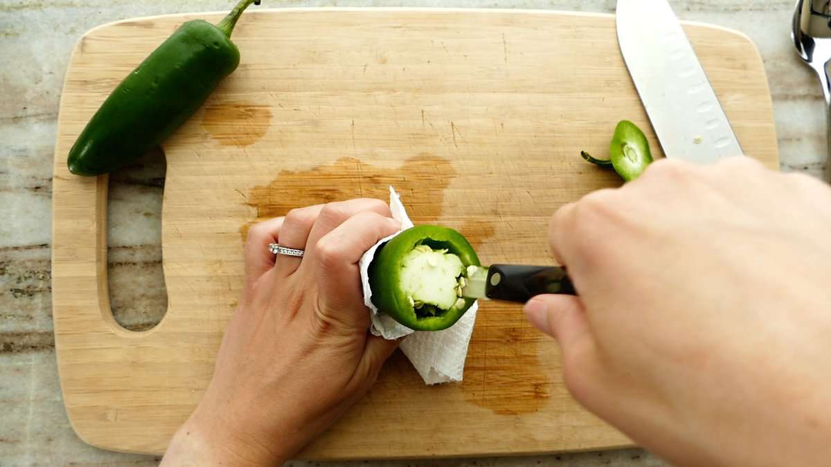 woman removing the seeds and membranes of a jalapeño pepper with a paring knife