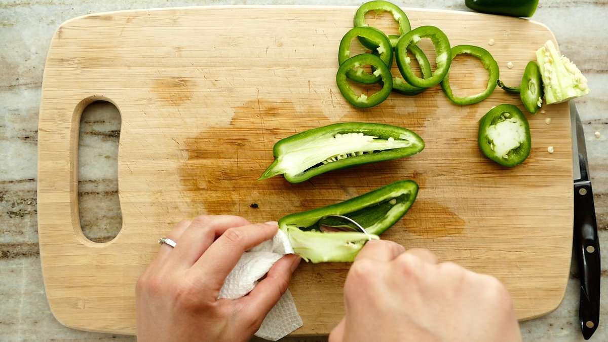 woman removing the seeds and membrane of a jalapeño with a paring knife