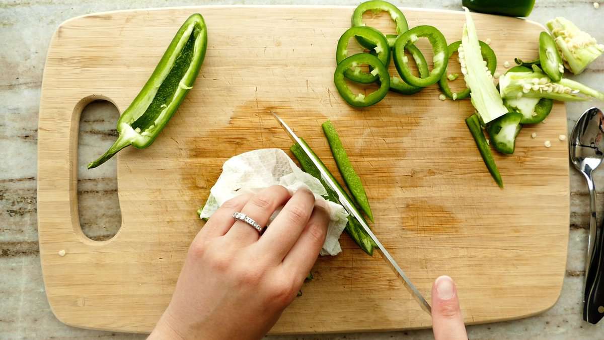 woman cutting a pepper into thin strips before dicing it