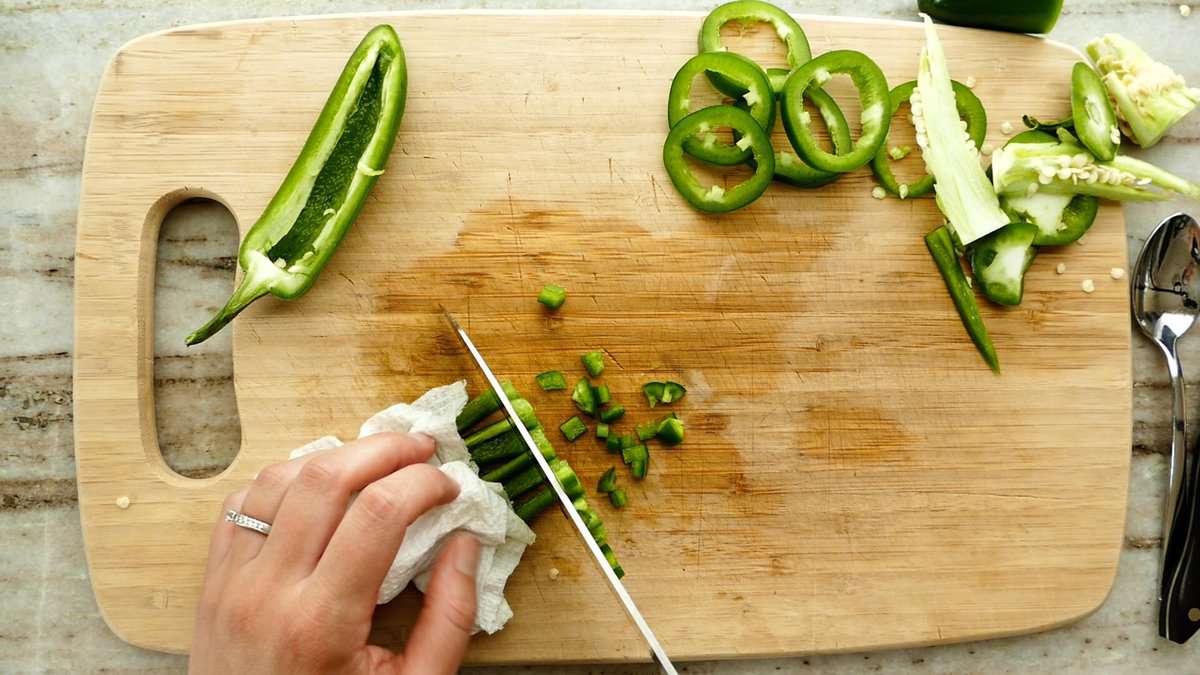 woman dicing a jalapeño into small pieces on a cutting board