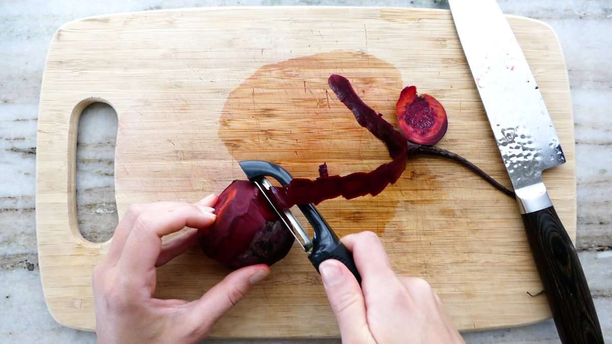 woman peeling a beet with a swivel peeler on a cutting board
