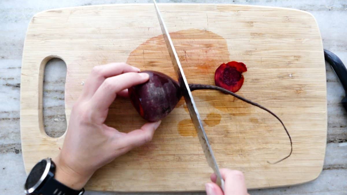 woman trimming the root of a beet with a chef's knife on a cutting board