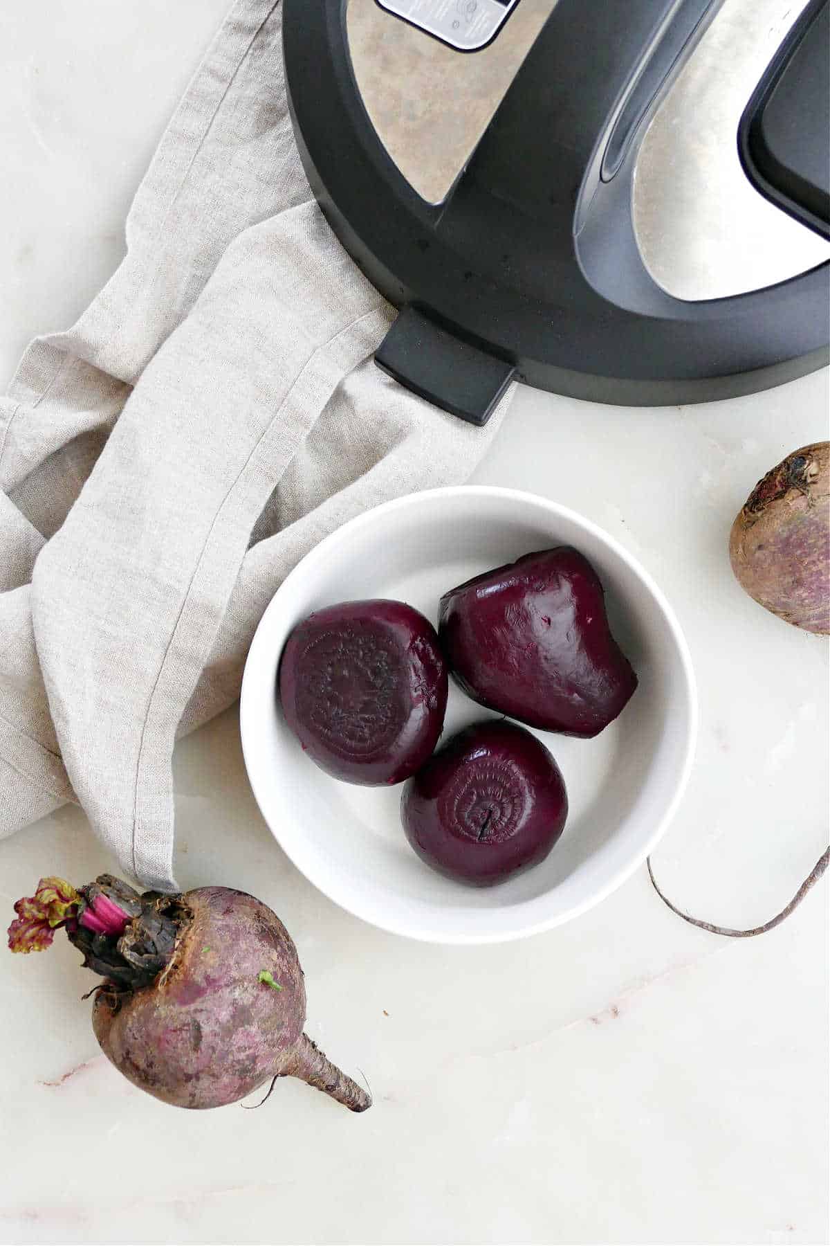 Instant Pot beets in a bowl next to raw beets and the Instant Pot lid