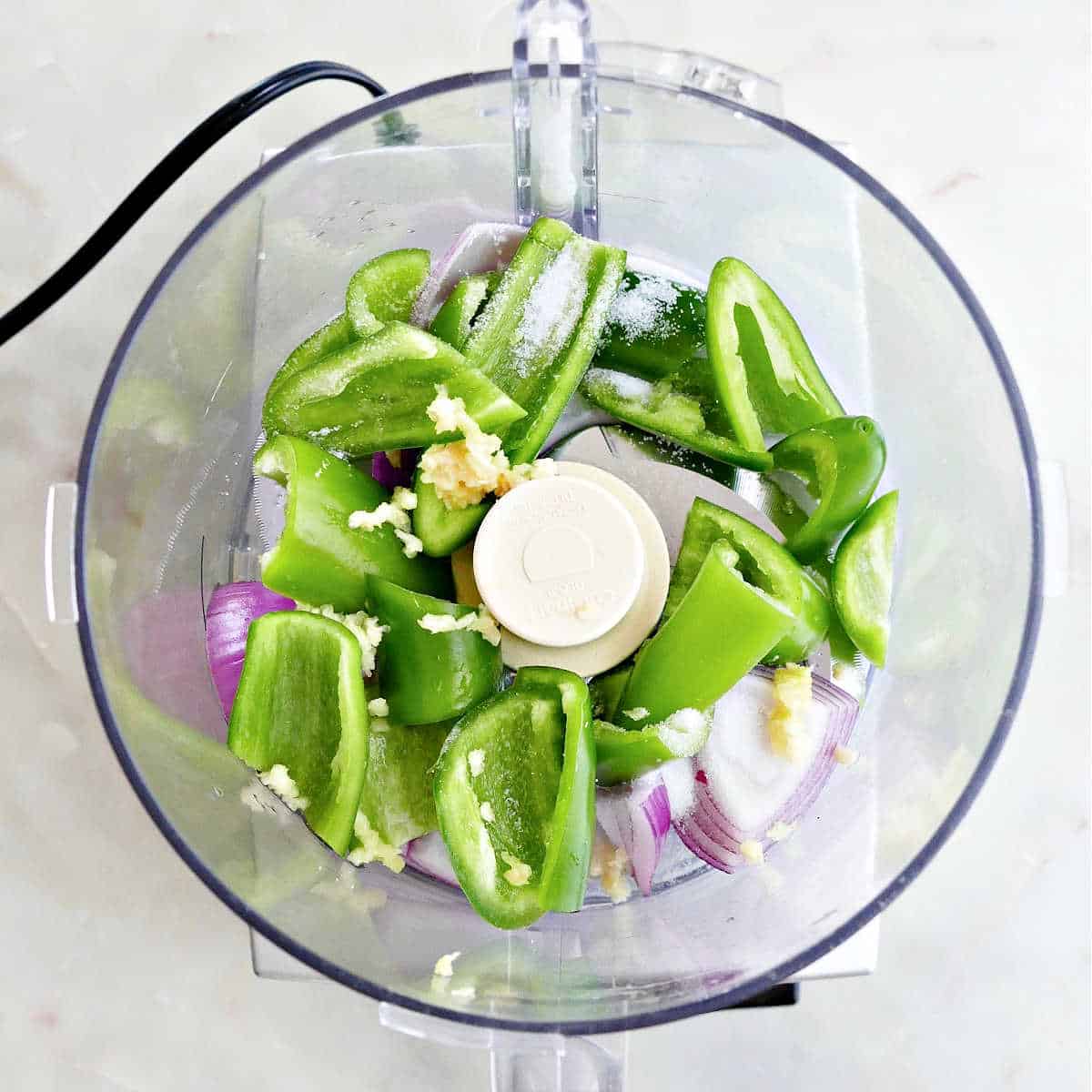 jalapeños, red onion, and garlic in a food processor on a counter