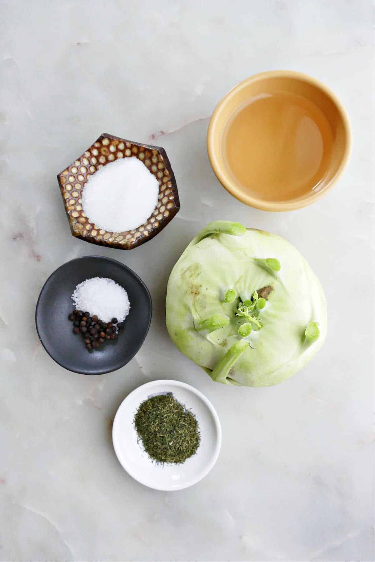 kohlrabi, vinegar, sugar, salt, peppercorns, and dried dill next to each other on a counter