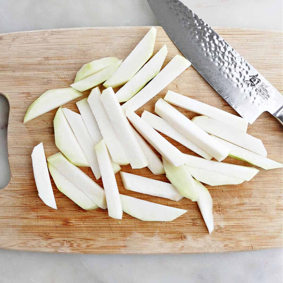 kohlrabi sliced into spears on a cutting board with a chef's knife