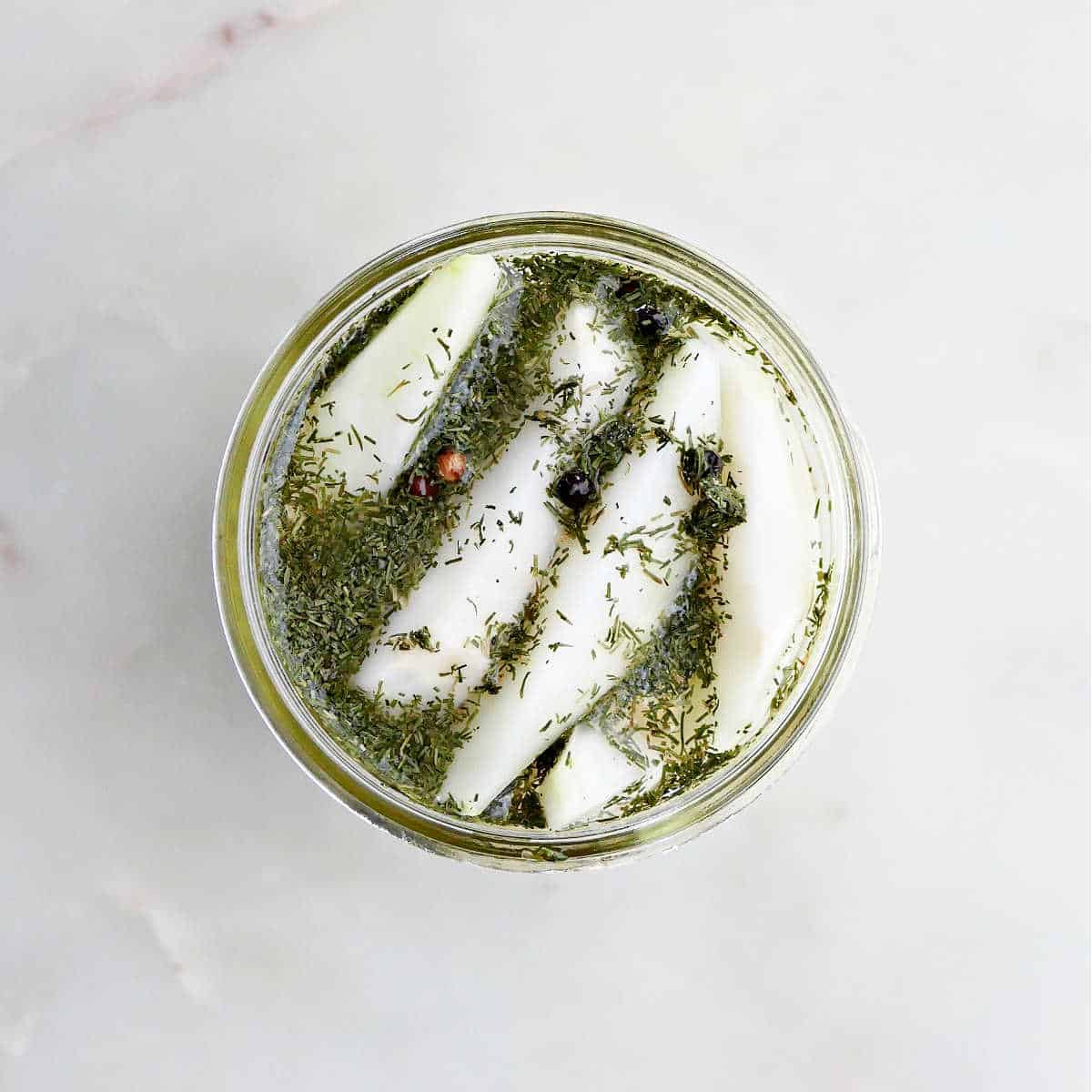 kohlrabi spears with brine poured over them in a glass jar on a counter