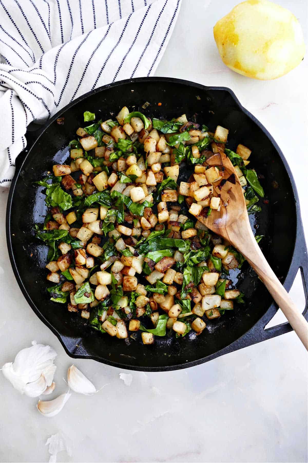 sautéed kohlrabi and greens in a cast iron skillet with a wooden spoon