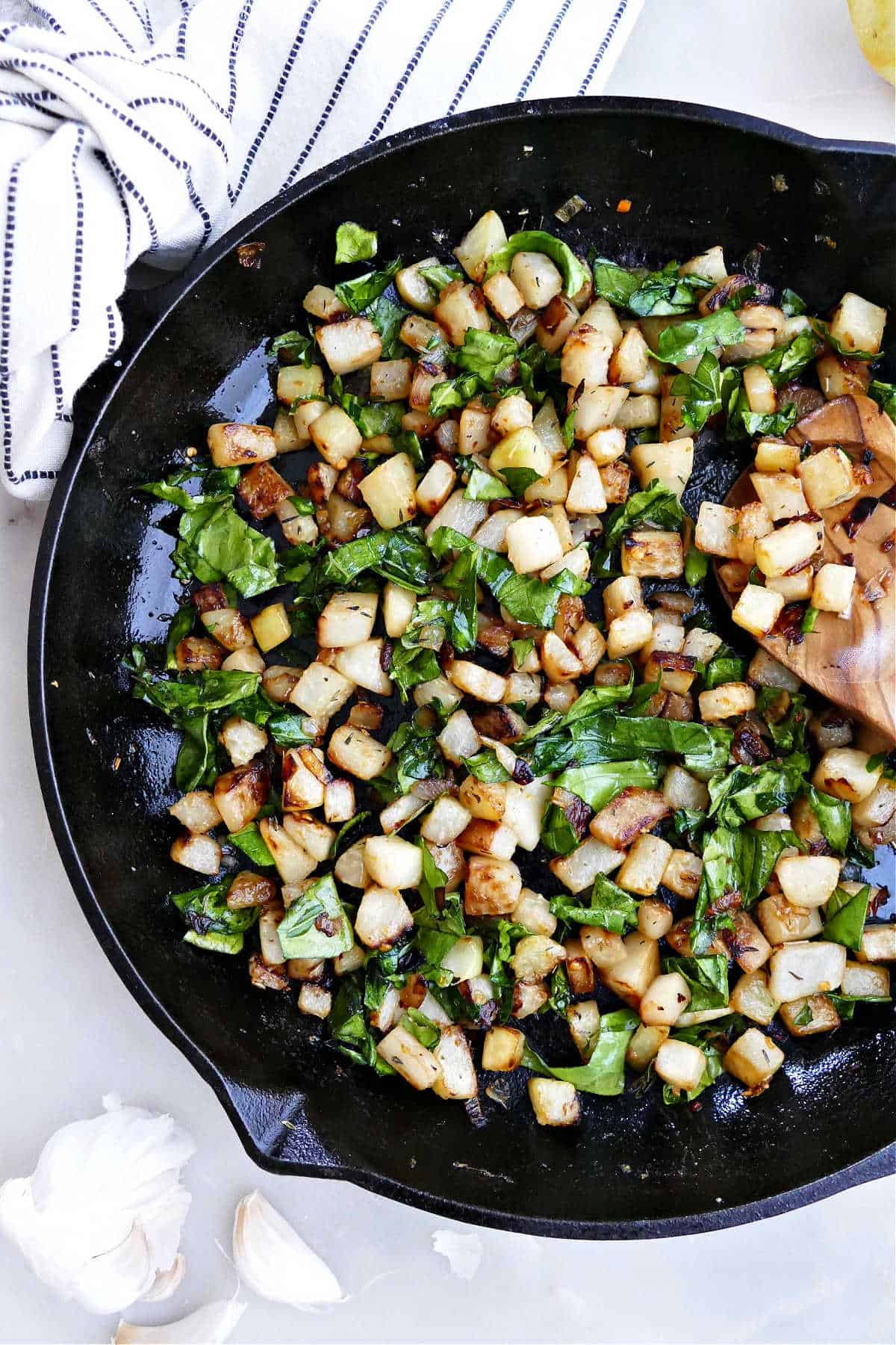 pan fried kohlrabi and kohlrabi leaves in a cast iron skillet with a spoon