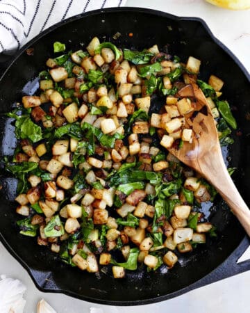 sautéed kohlrabi and greens in a cast iron skillet with a wooden spoon