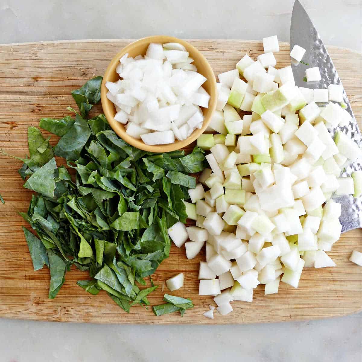 chopped kohlrabi bulb, leaves, and onion on a cutting board with a knife