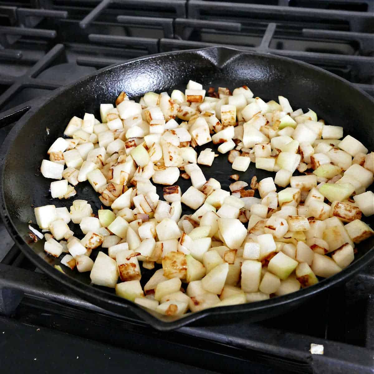 kohlrabi and onion cooking in a cast iron skillet over a stove
