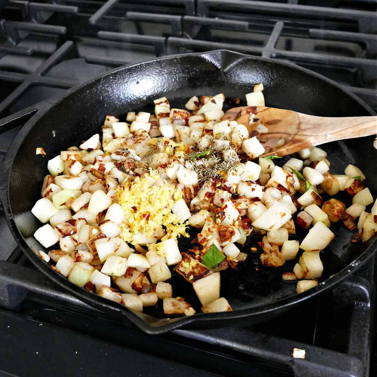 kohlrabi, onion, lemon zest, and spices cooking in oil in a cast iron skillet