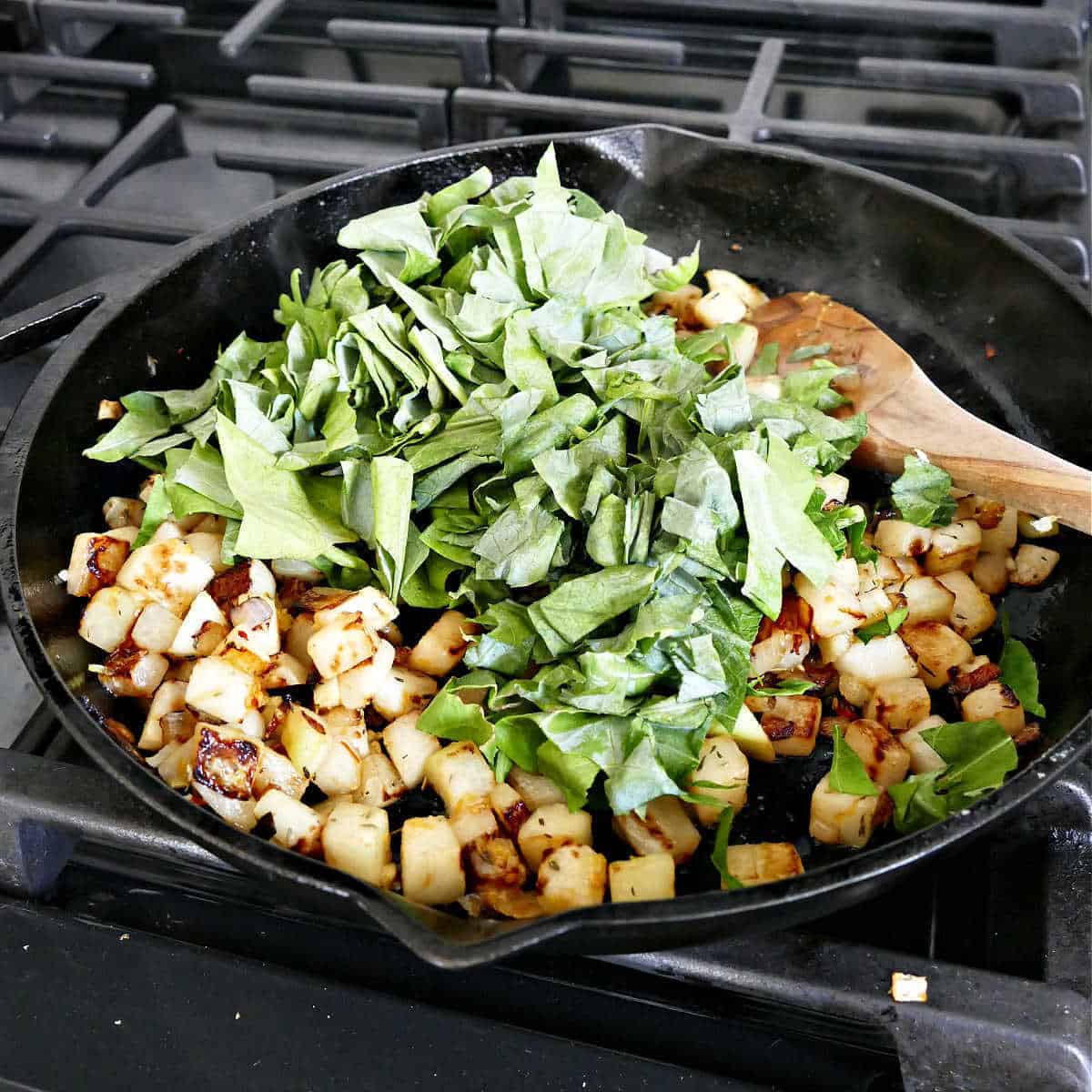 sautéed kohlrabi cooking in a cast iron skillet with the leaves being added