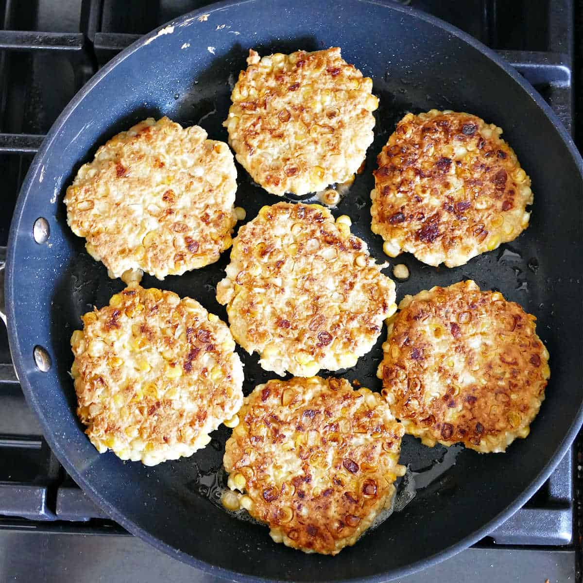 corn fritters being fried in olive oil in a skillet on the stove