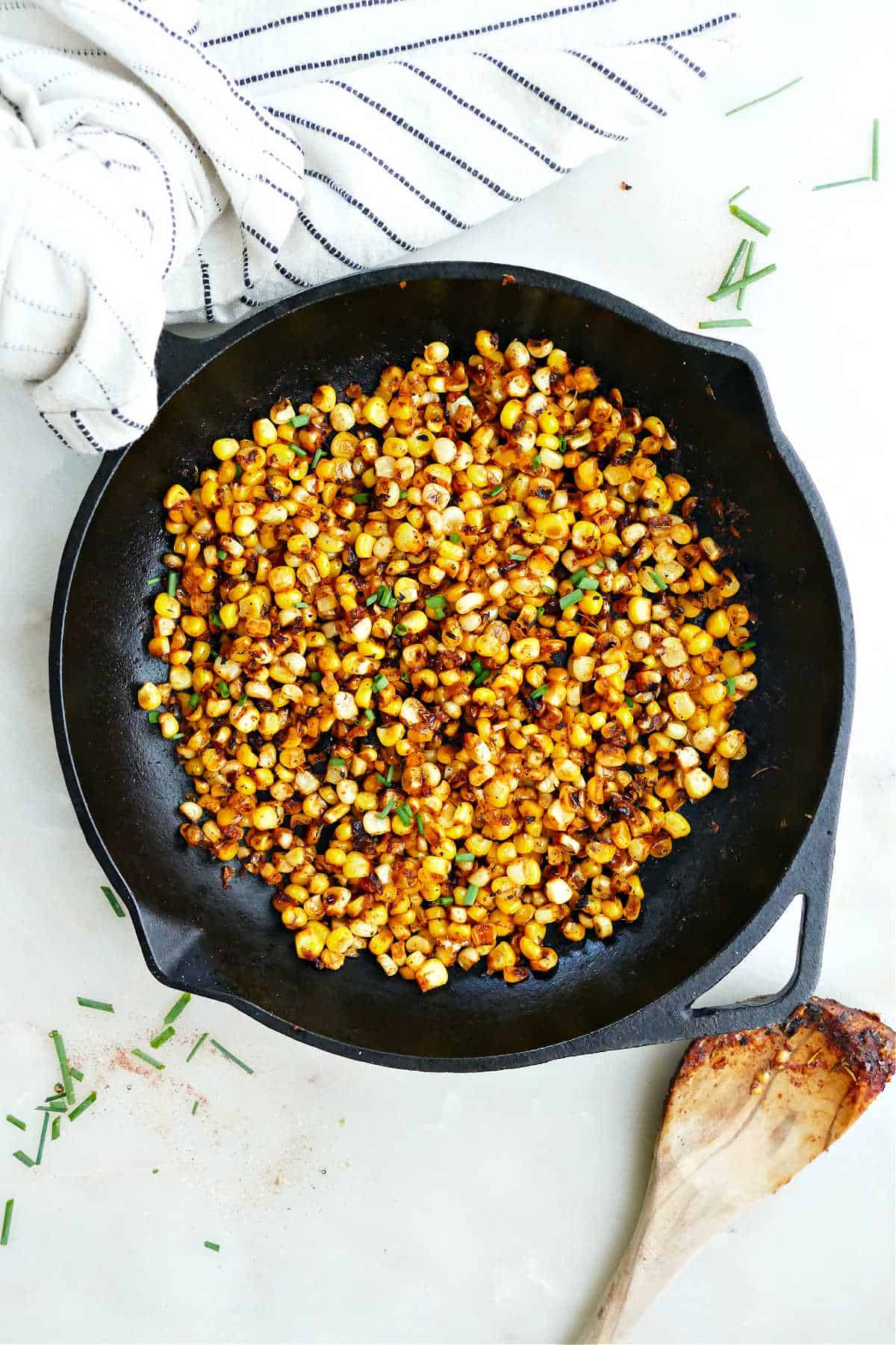 blackened corn in a skillet next to a spoon and napkin