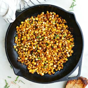 blackened corn in a skillet next to a spoon and napkin