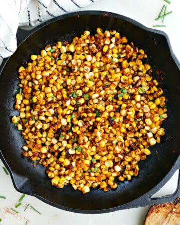 blackened corn in a skillet next to a spoon and napkin