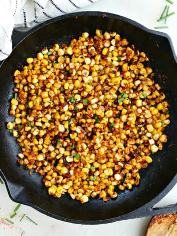 blackened corn in a skillet next to a spoon and napkin