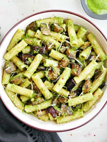 eggplant pesto pasta in a serving bowl next to ingredients and a napkin