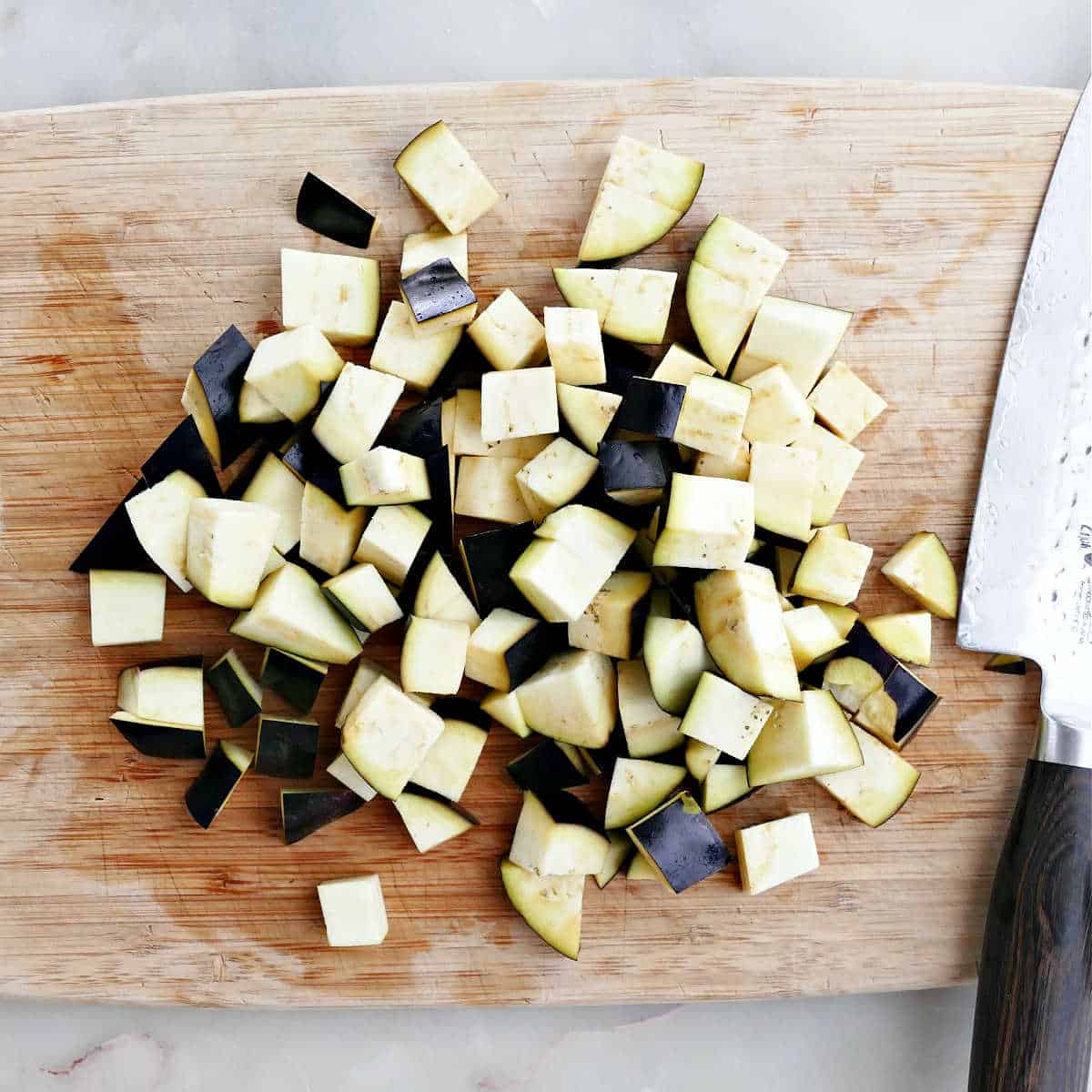 eggplant cut into cubes on a cutting board with a knife
