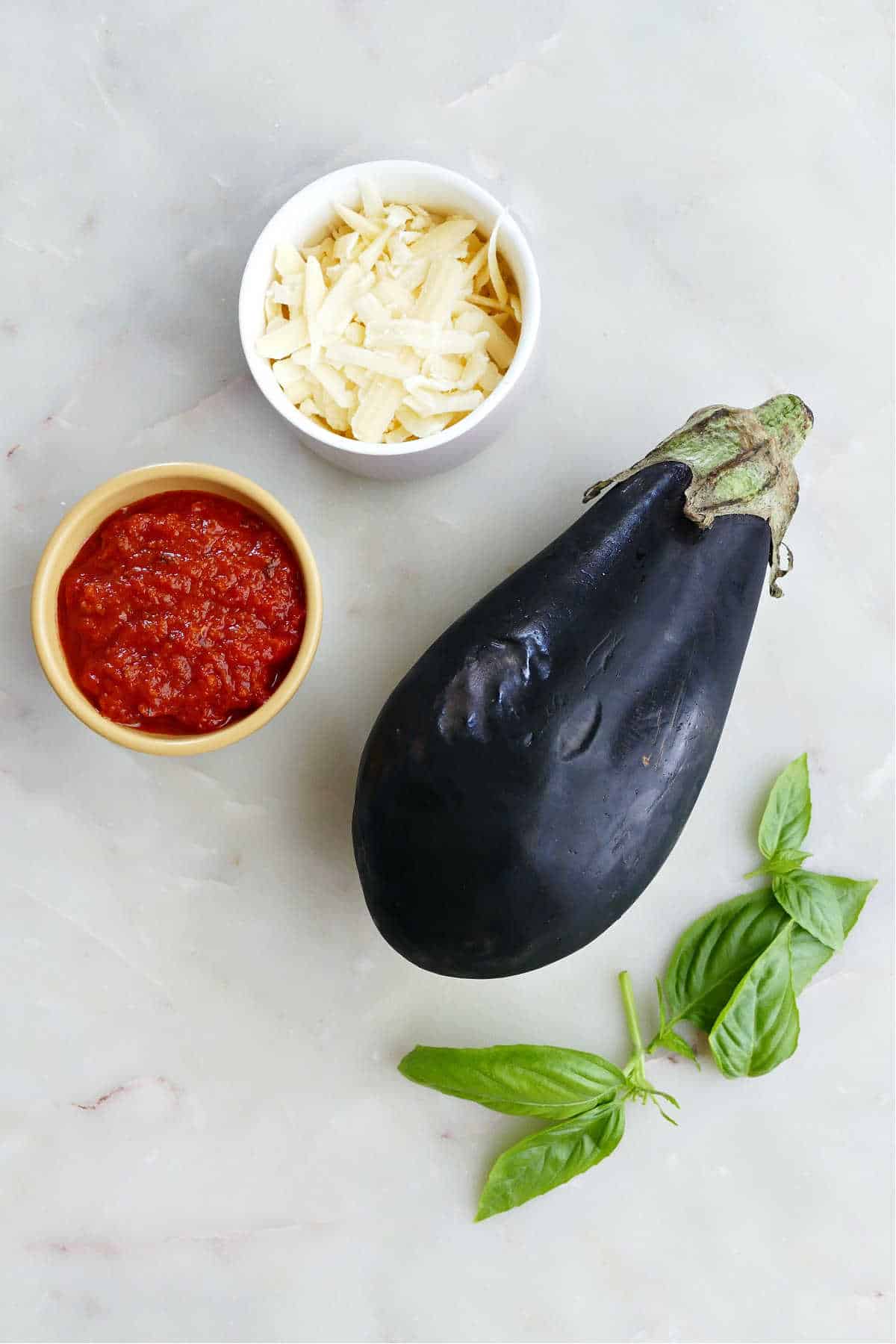 pizza sauce, shredded cheese, eggplant, and basil on a counter