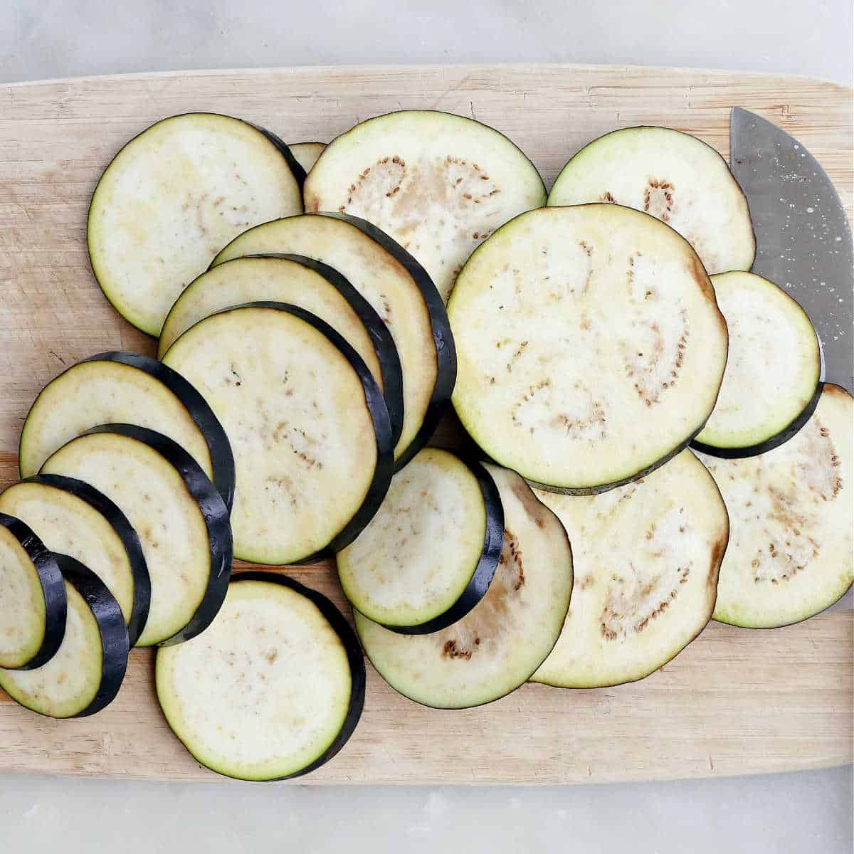 sliced eggplant rounds on a bamboo cutting board next to a knife