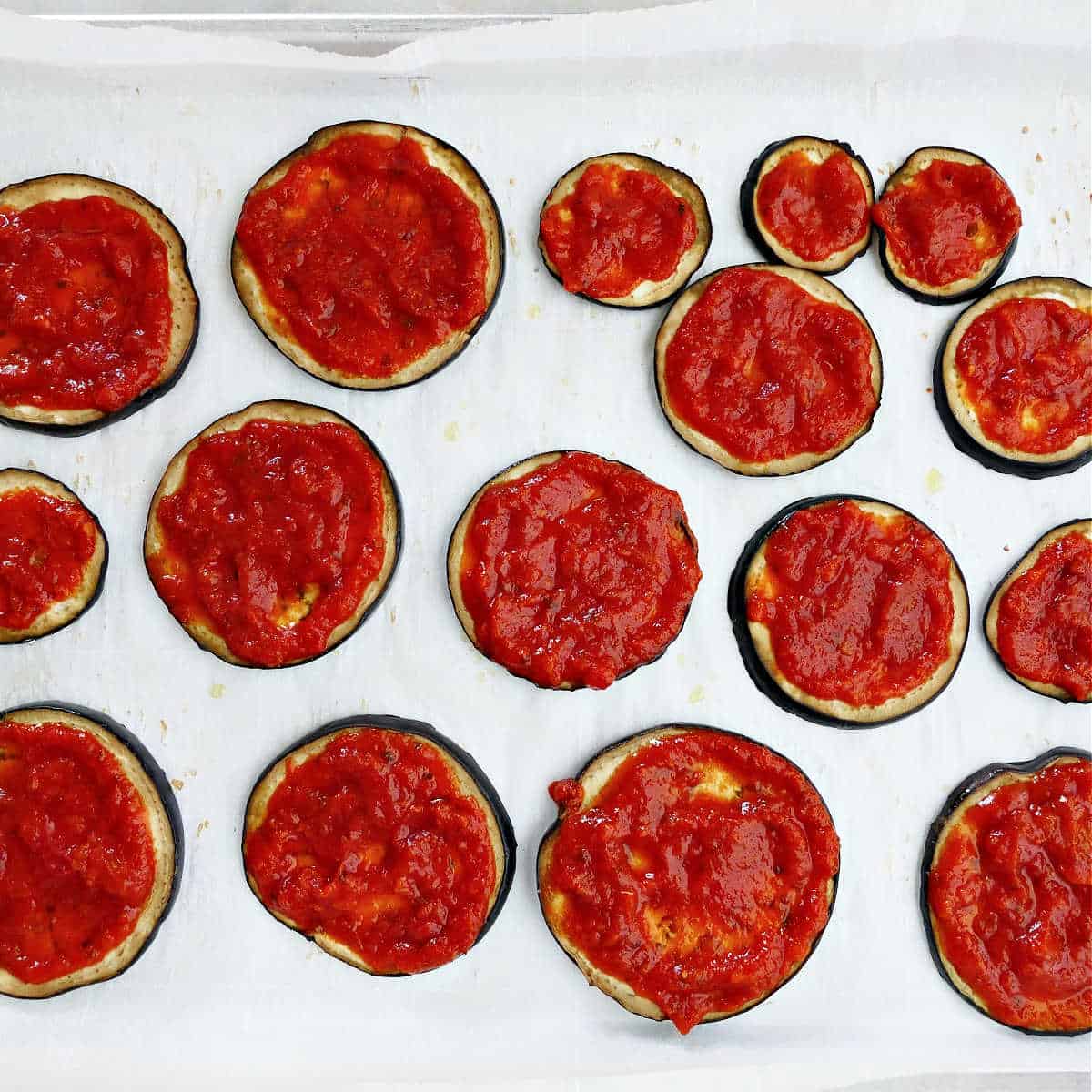 eggplant rounds topped with tomato sauce on a baking sheet