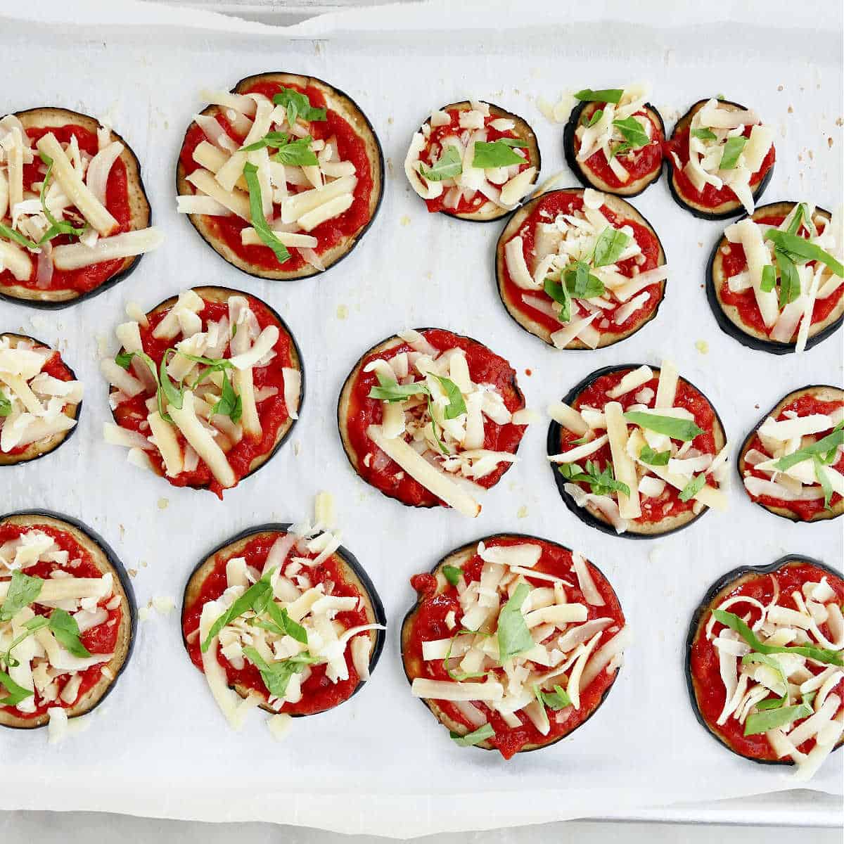 eggplant slices topped with tomato sauce, cheese, and basil on a baking sheet
