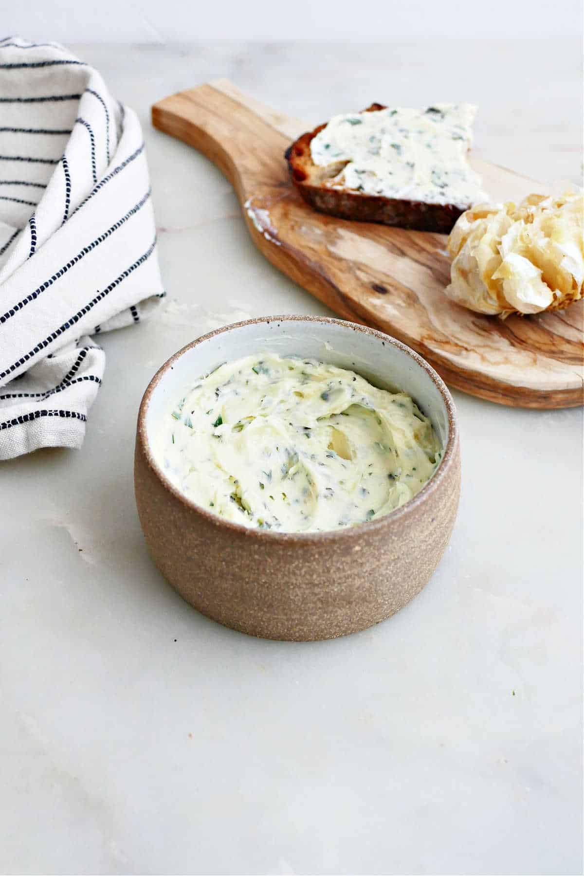 garlic herb butter in a bowl in front of a board with bread and a napkin
