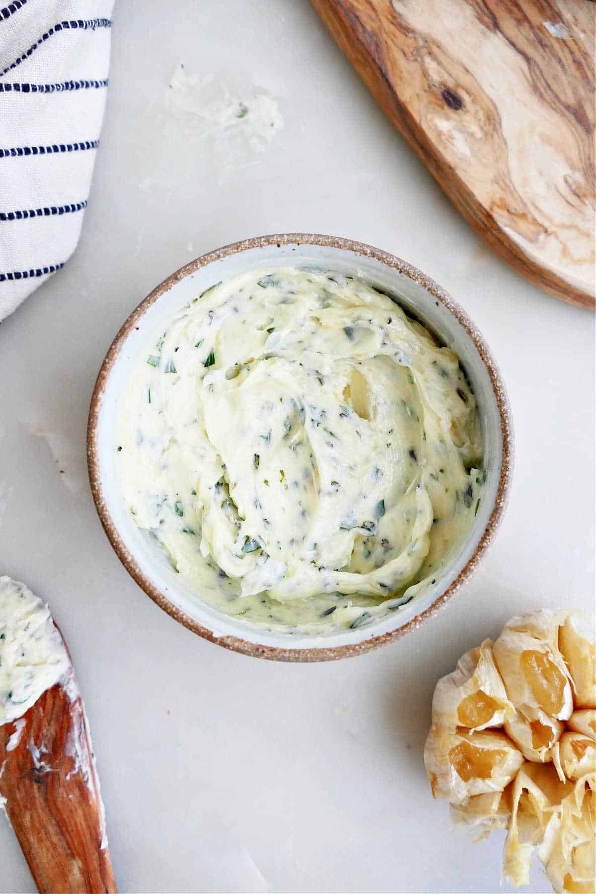 roasted garlic butter in a bowl next to napkin, board, roasted garlic, and a knife