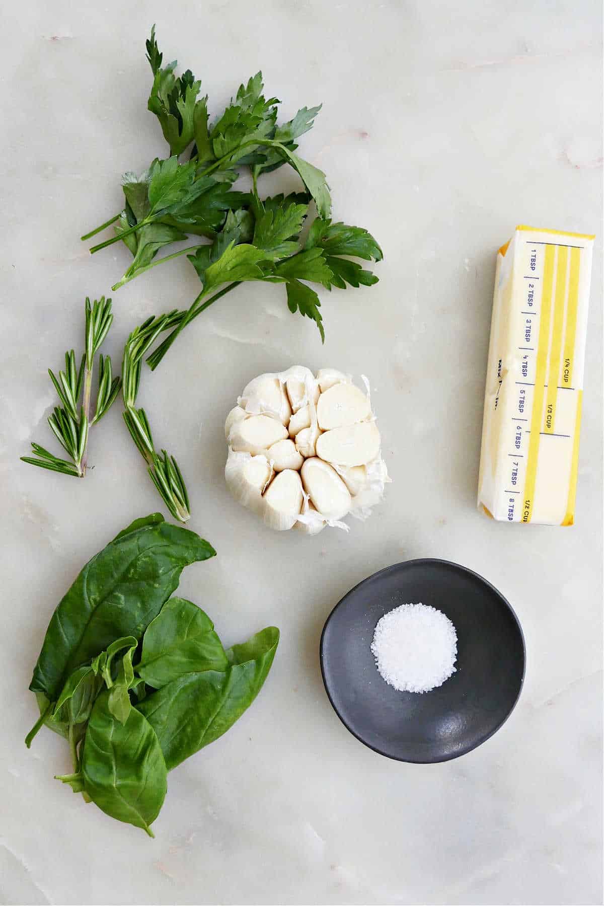 parsley, rosemary, basil, garlic, salt, and butter on a counter