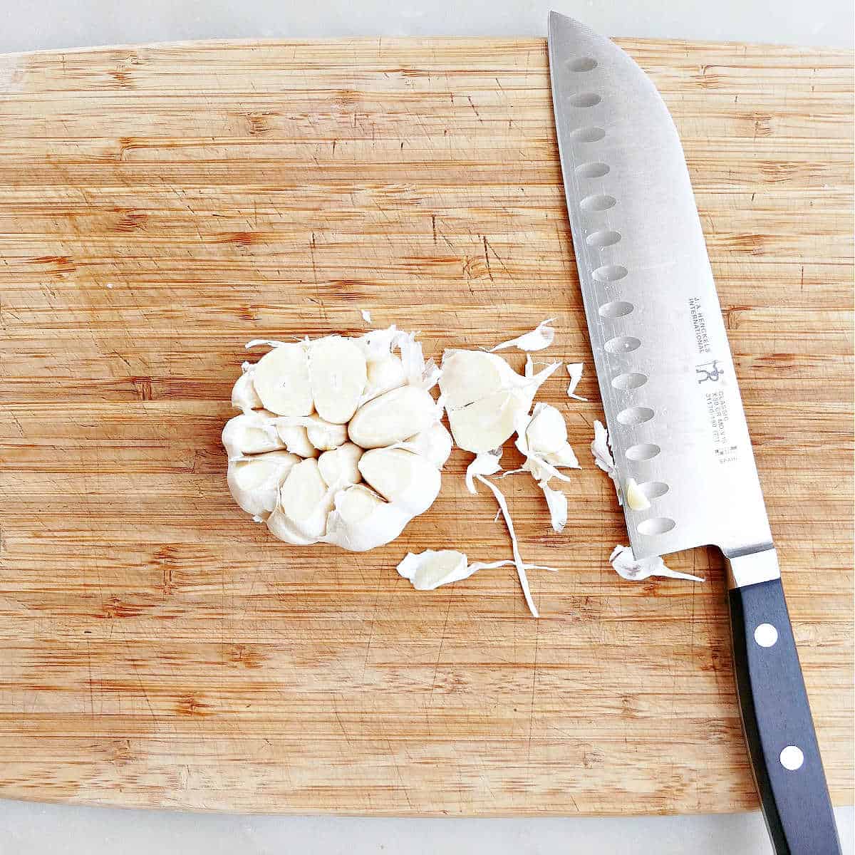 head of garlic being trimmed before roasting on a cutting board