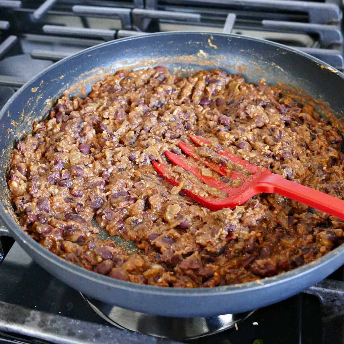 smashed black bean filling for tacos in a skillet with a large silicone fork