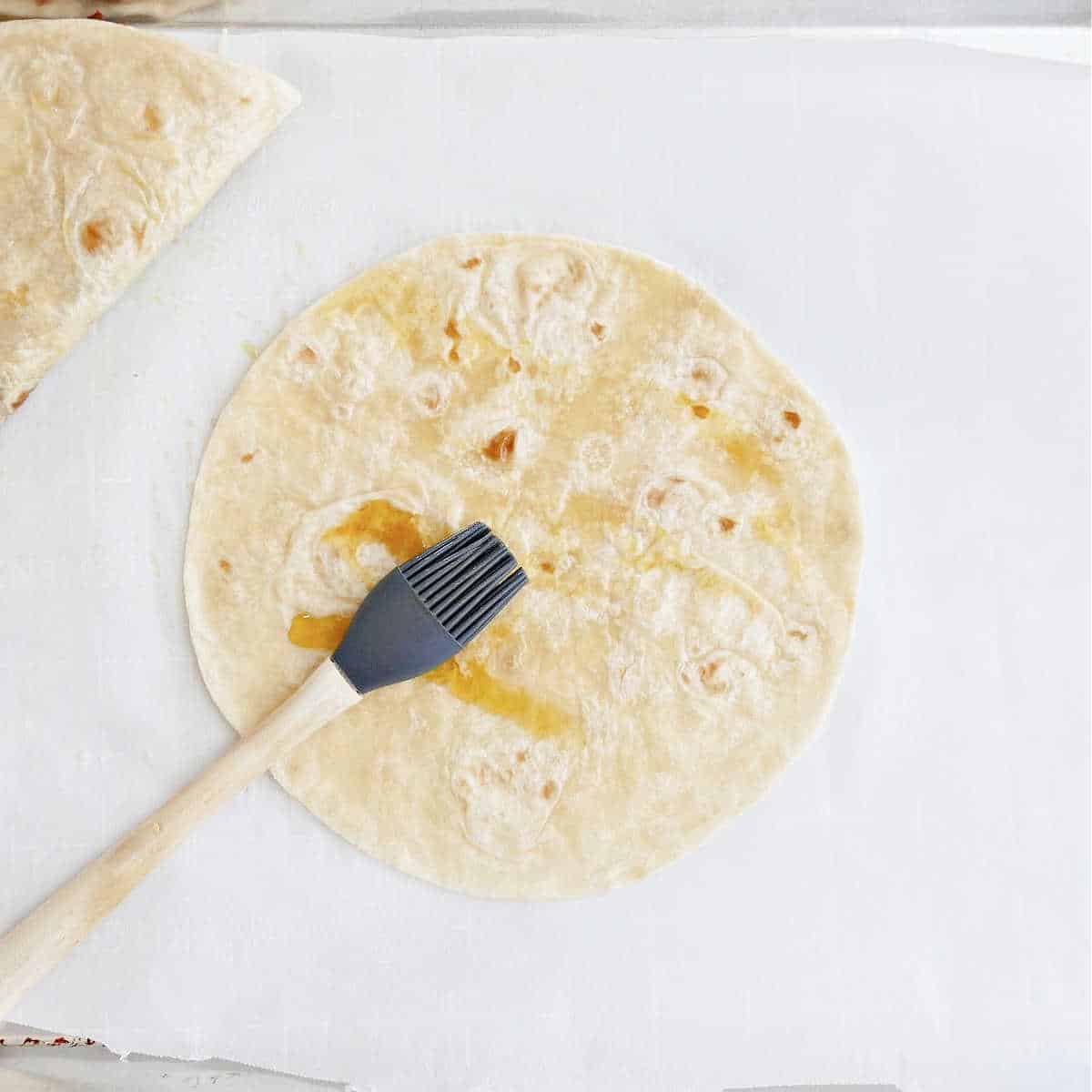 flour tortilla being brushed with oil on a baking sheet