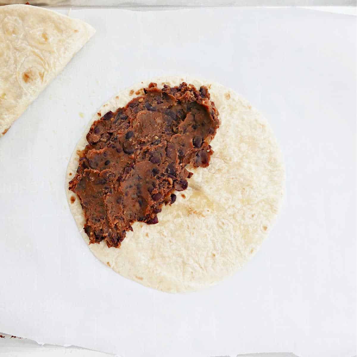 tortilla with black bean filling on a lined baking sheet