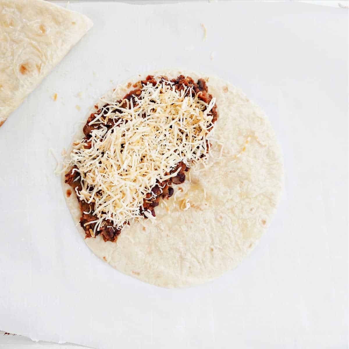 tortilla with black bean filling and shredded cheese on a baking sheet